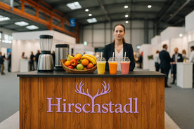 Smoothie-Bar in einer Messehalle: Mixer, Obstschale und Säfte auf der Holztheke, dahinter eine Mitarbeiterin